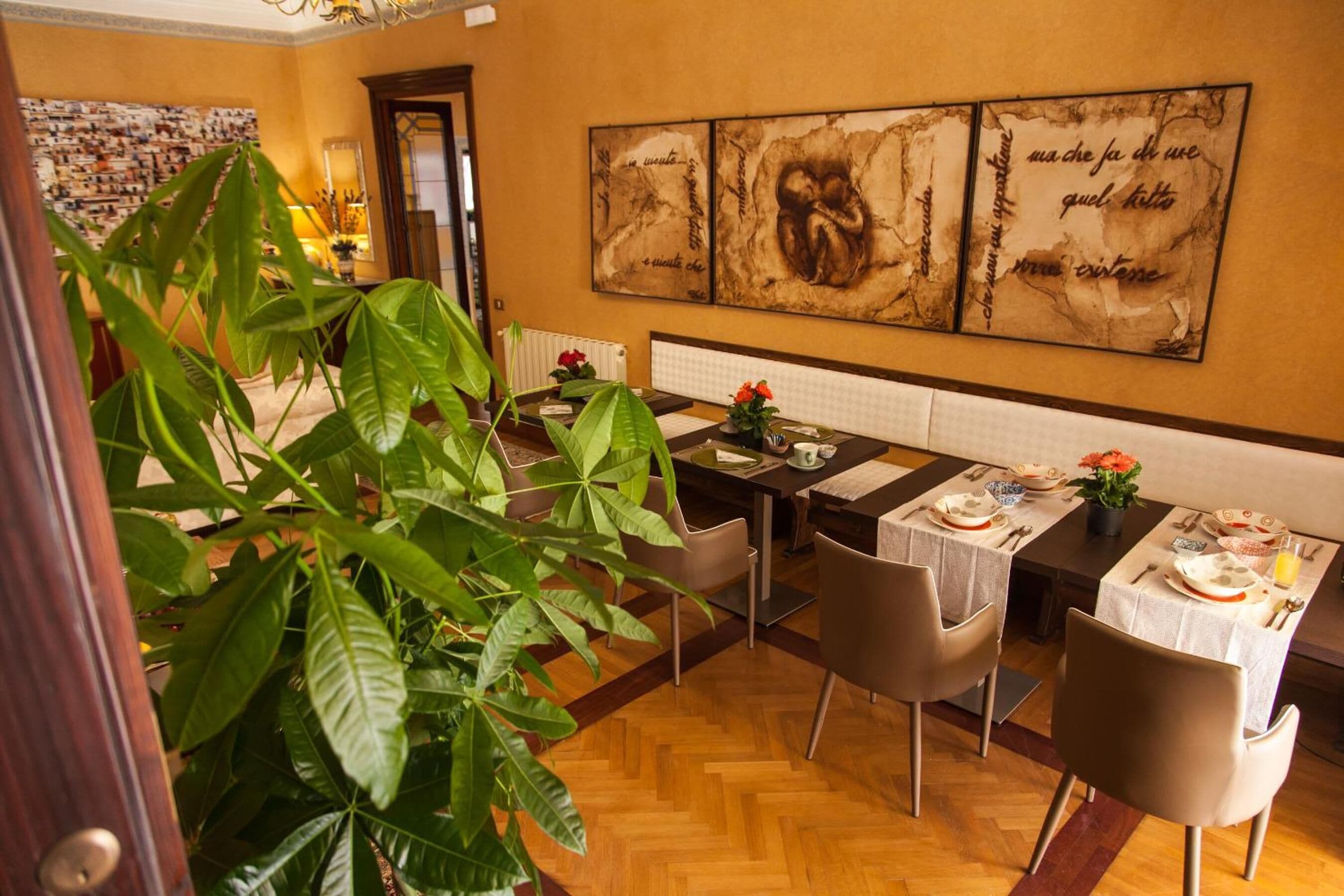 A dining area with a wooden floor, a large potted plant, and a table set for four.