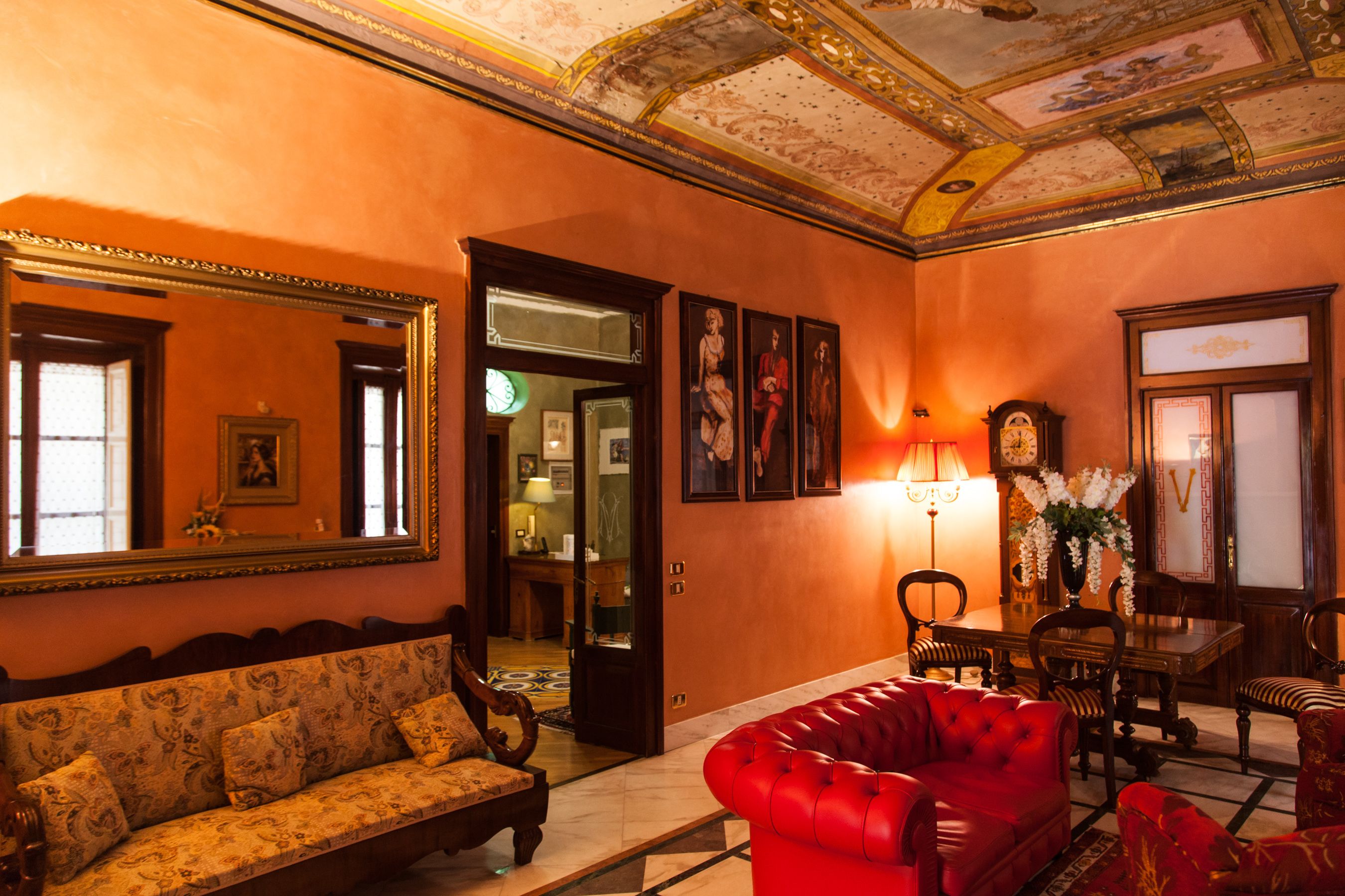A room with a sofa, a red armchair, a table with chairs, a mirror, and a chandelier.