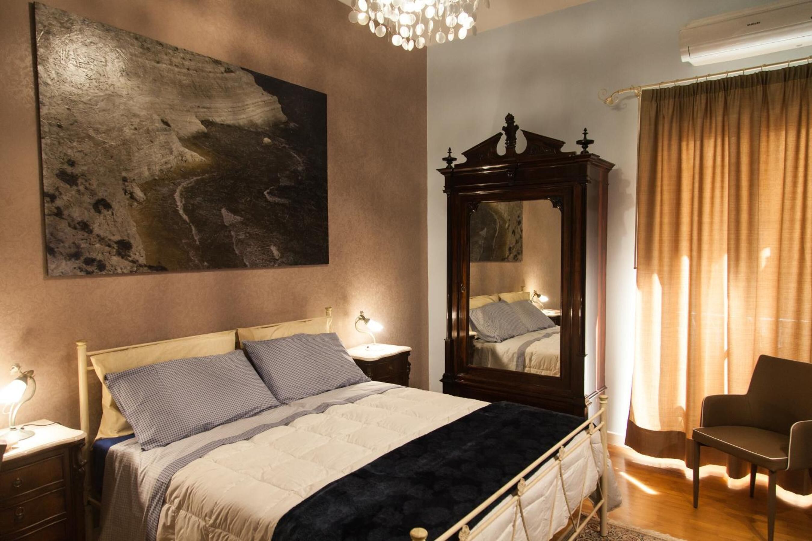 Un dormitorio con una cama grande, una mesita de noche de madera, un espejo, una silla y un cuadro en la pared.