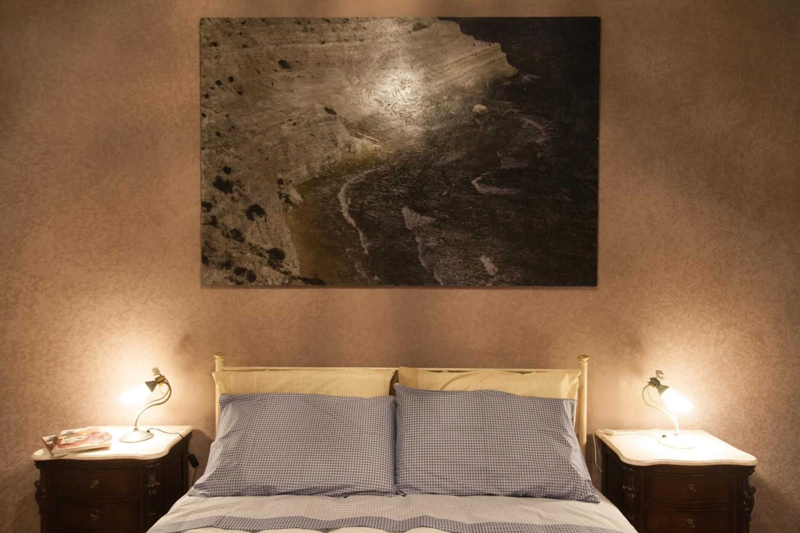 Un dormitorio con cama, dos mesitas de noche con lámparas y un cuadro abstracto grande en la pared.