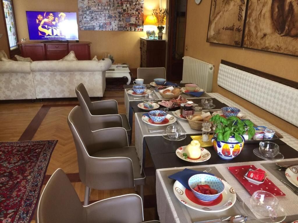 A dining area with a table set for four, surrounded by modern chairs. A television is mounted on the wall in the background.