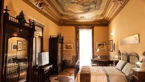 Una habitación con una cama grande, un escritorio, una silla, un espejo y un techo con diseños intrincados.