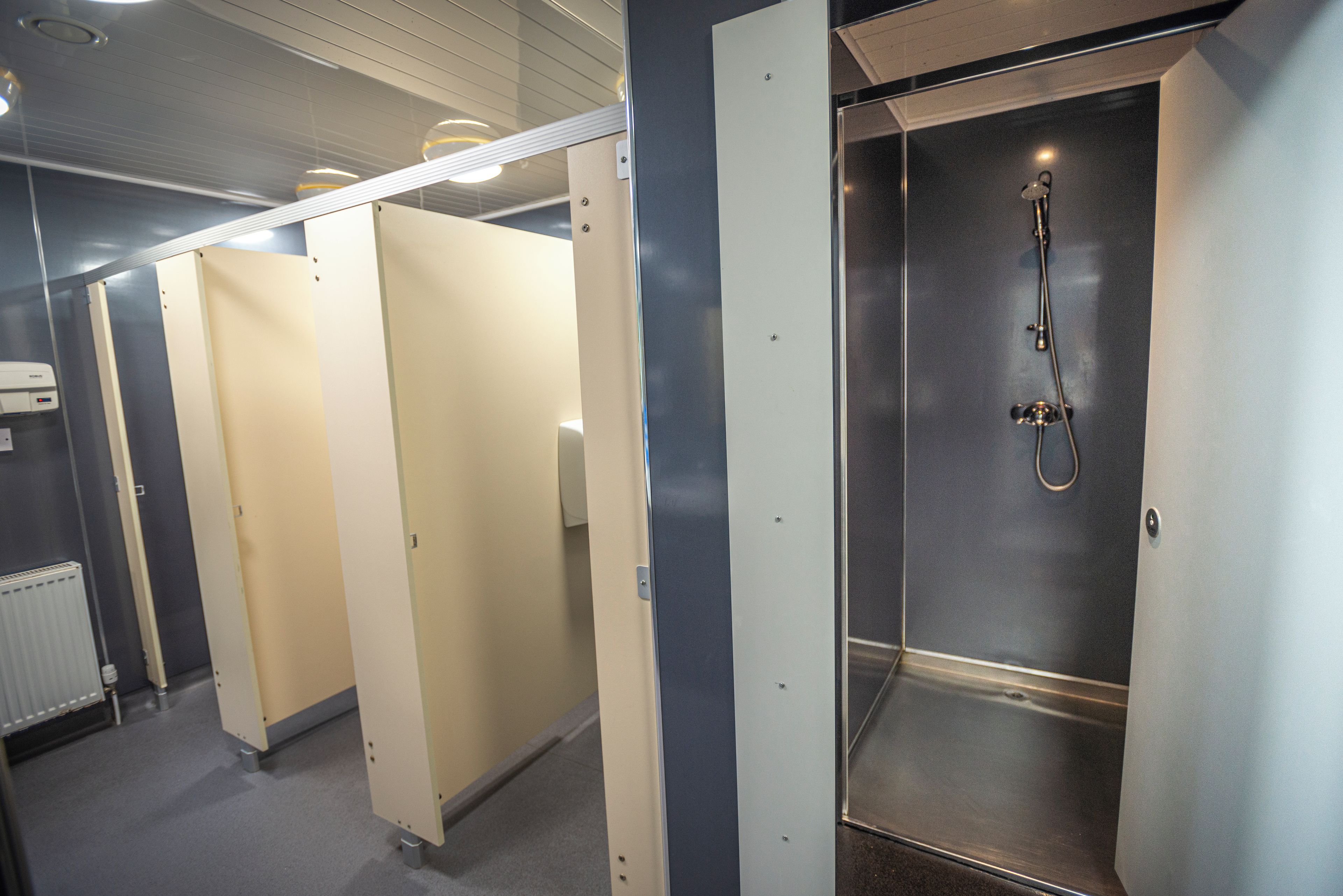 Een rij van afgeschermde douchecabines met een handdroger en een handdoekdispenser.