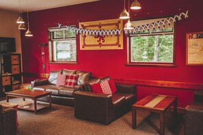 A cozy room with a red wall, a leather sofa, a wooden coffee table, and a bookshelf. - Crianlarich Youth Hostel (Crianlarich)