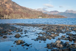 A rocky shoreline with a house on a hill in the background. - Crianlarich Youth Hostel (Crianlarich)