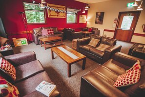 A cozy lounge area with leather sofas, wooden tables, and a red accent wall. - Crianlarich Youth Hostel (Crianlarich)