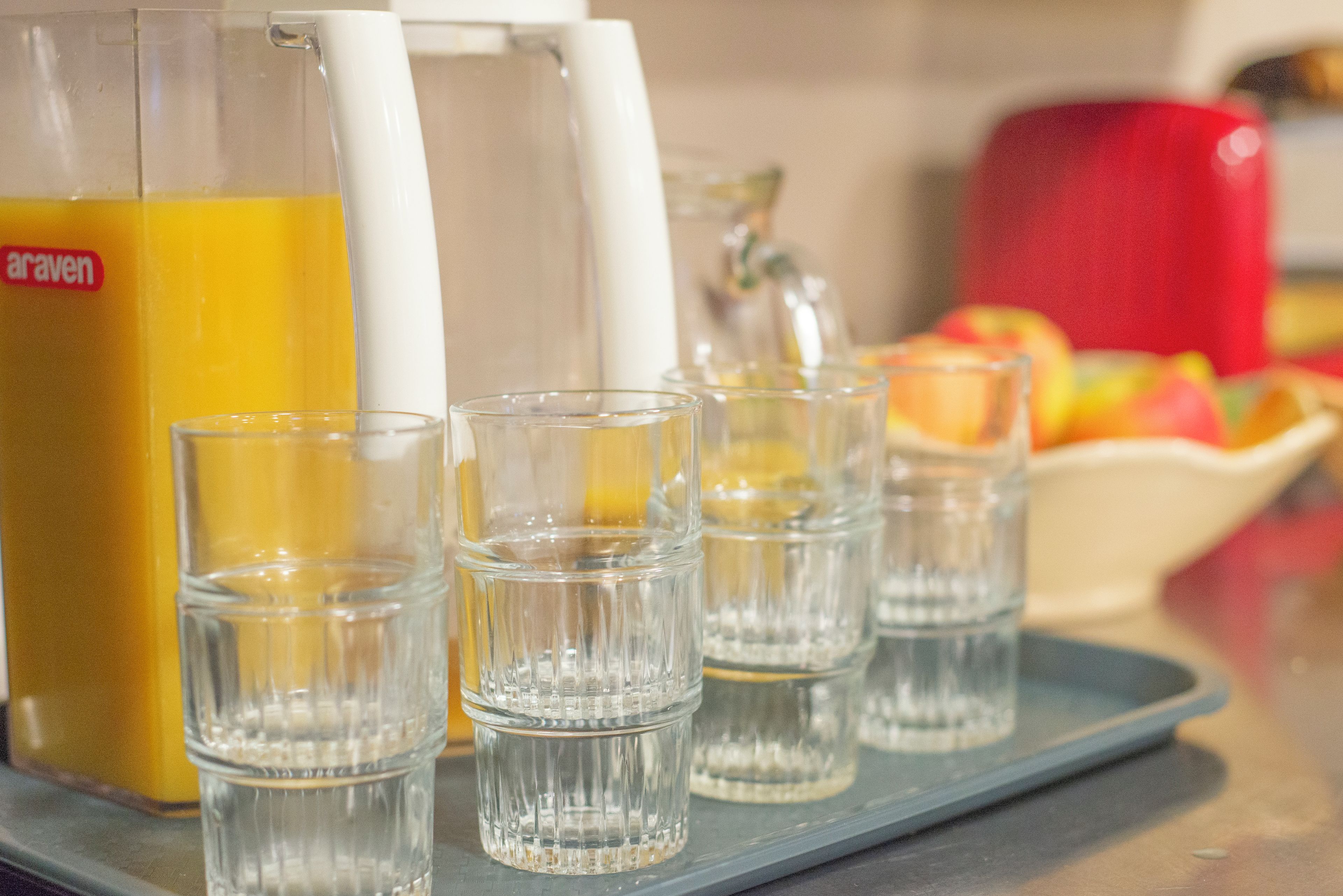 Una encimera de cocina con dispensador de jugo y vasos para chupitos.