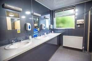 Baño público con dos lavamanos, secamanos y una ventana.
