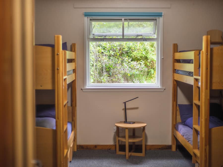 A room with bunk beds, a small table, and a window with a view of greenery.