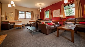 A living room with leather sofas, wooden coffee tables, and pendant lighting. - Crianlarich Youth Hostel (Crianlarich)