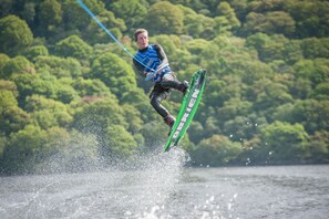Una persona pratica wakeboard su un lago con uno sfondo boschivo.