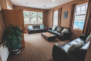 A furnished living room with a sofa, armchairs, a coffee table, and a potted plant. - Lochranza Youth Hostel (Isle of Arran)
