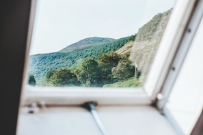 Vista desde una ventana a un paisaje montañoso con abundante vegetación y cielo despejado.
