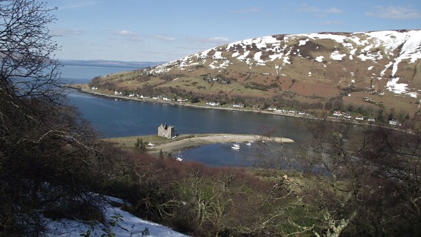 A coastal landscape with a castle-like structure near a body of water, surrounded by hills and sparse vegetation. - Lochranza Youth Hostel (Isle of Arran)