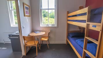 A bunk bed room with a desk and chair, a radiator, and a window with a view of greenery.