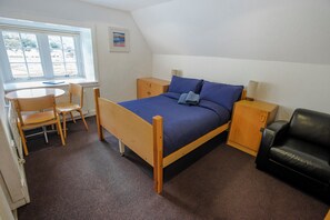 A bedroom with a bed, a desk, a chair, a wardrobe, and a black leather chair. - Lochranza Youth Hostel (Isle of Arran)