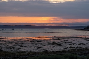 A coastal landscape with boats on calm waters, a beach with pebbles, and distant hills. - Lochranza Youth Hostel (Isle of Arran)