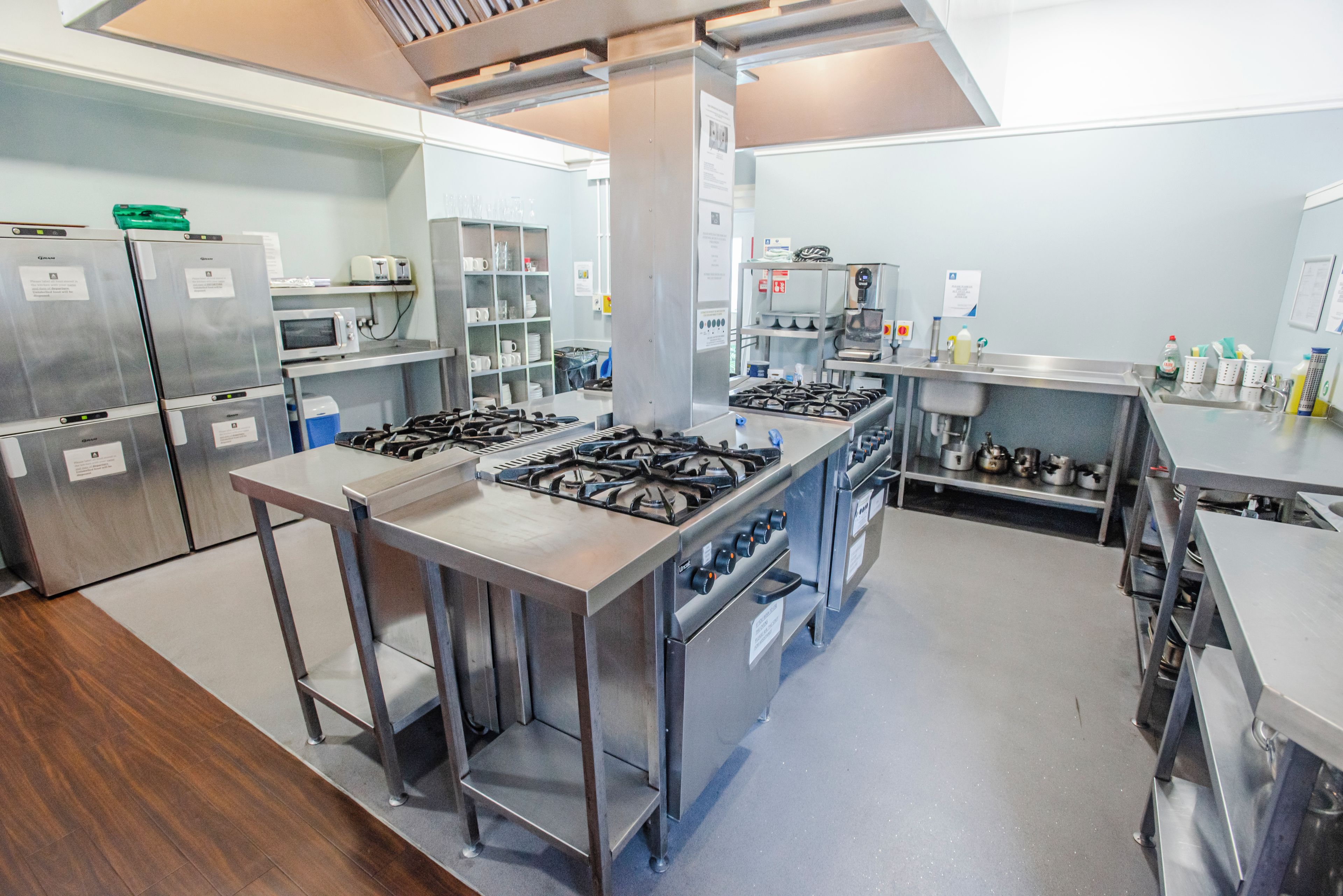 A commercial kitchen with stainless steel appliances, including a range, ovens, and a microwave.