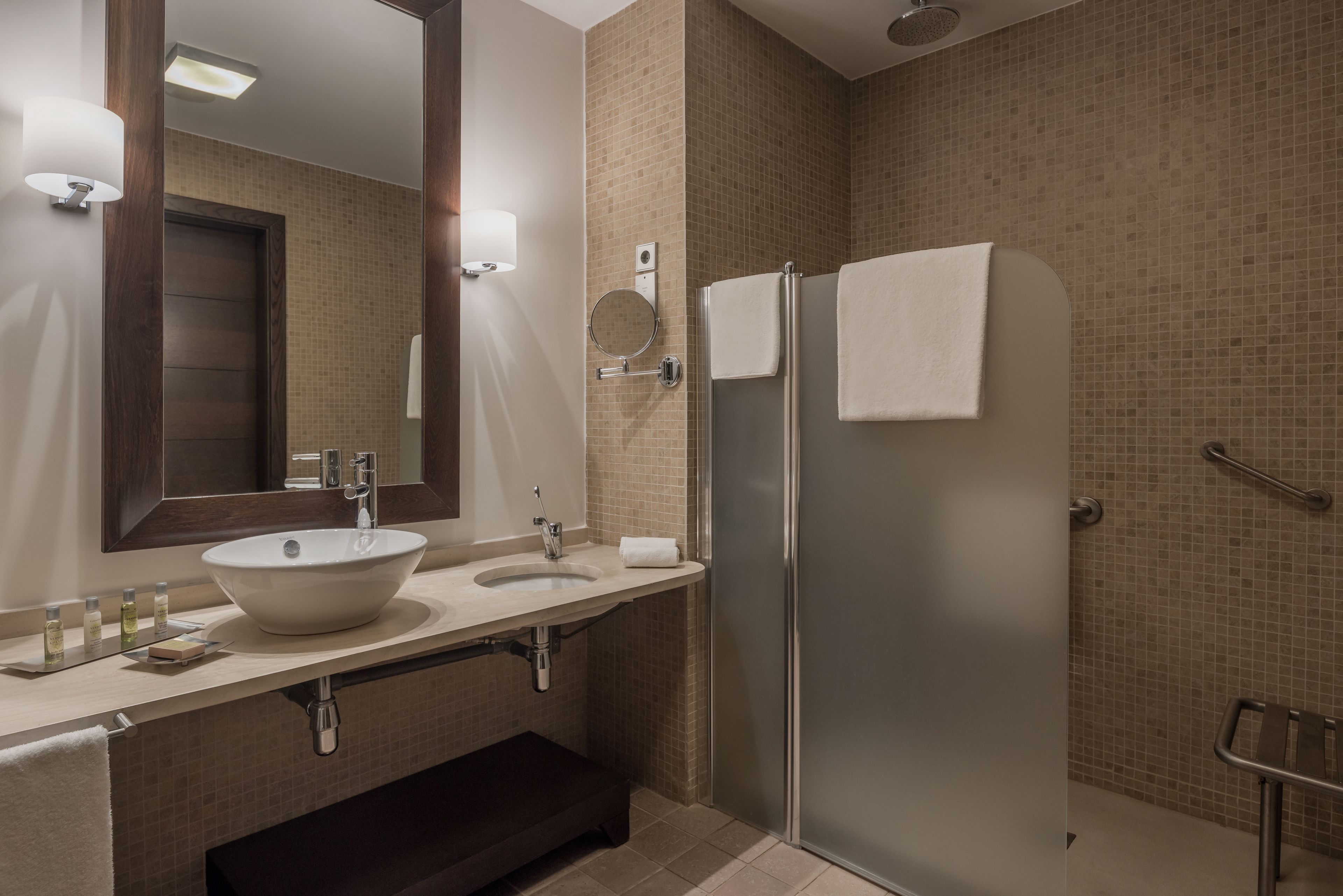 A modern bathroom with a large sink, a mirror, a towel rack, and a shower area.