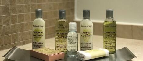 Una encimera de baño con cinco botellas de productos de cuidado corporal Verbenal de Crabtree & Evelyn, una pastilla de jabón y una toalla.