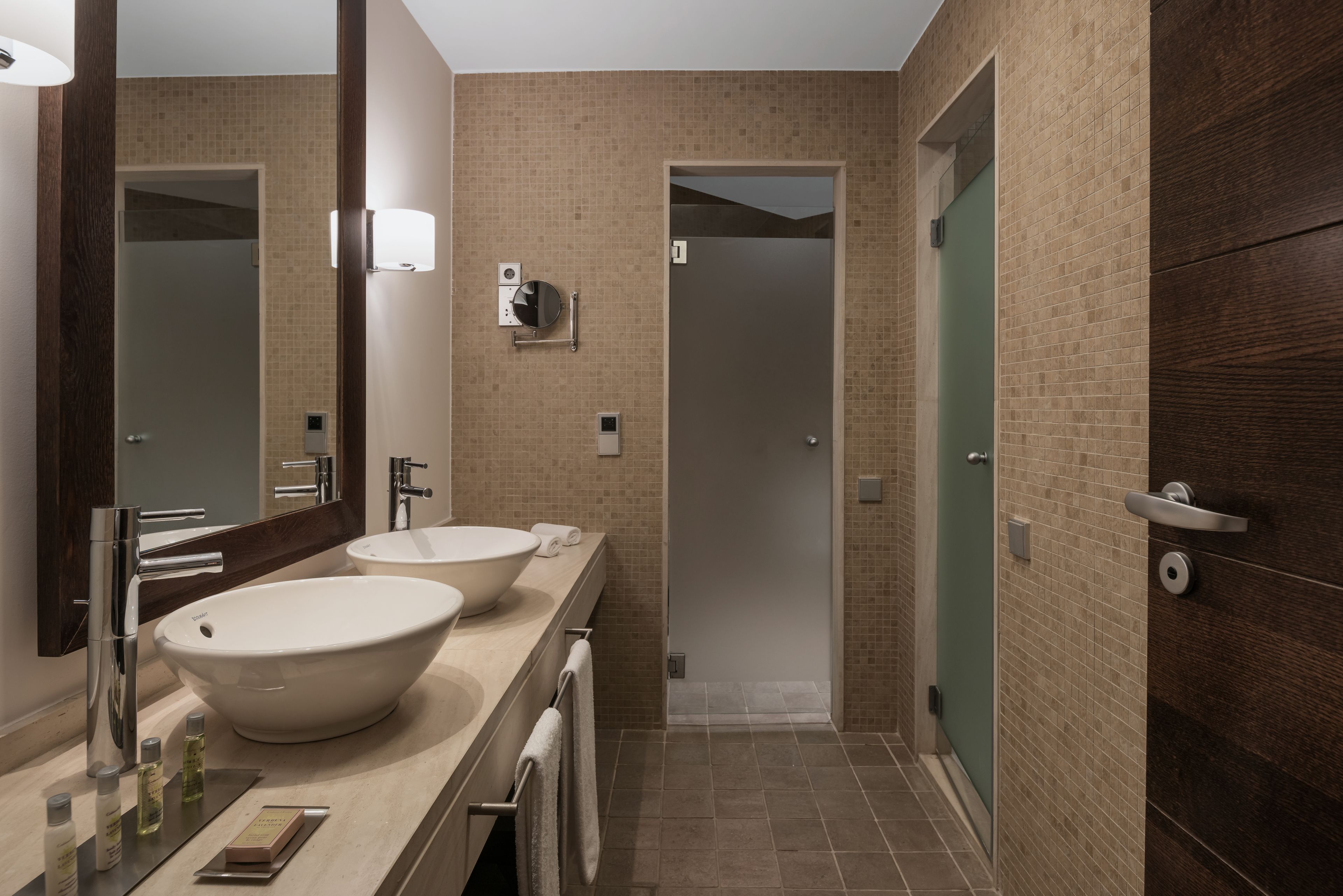 A modern bathroom with two large sinks, a mirror, and a walk-in shower.