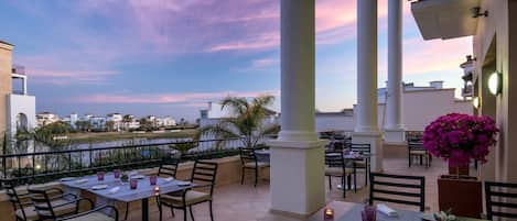 A rooftop dining area with tables and chairs, a view of the city, and a large column.