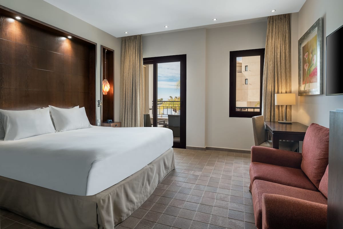 A hotel room with a large bed, a desk, a chair, and a view of the outside.