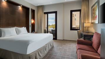 A hotel room with a large bed, a desk, a chair, and a view of the outside.