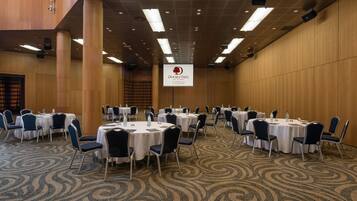 A conference room with round tables and chairs, a wooden wall, and a ceiling with recessed lighting.