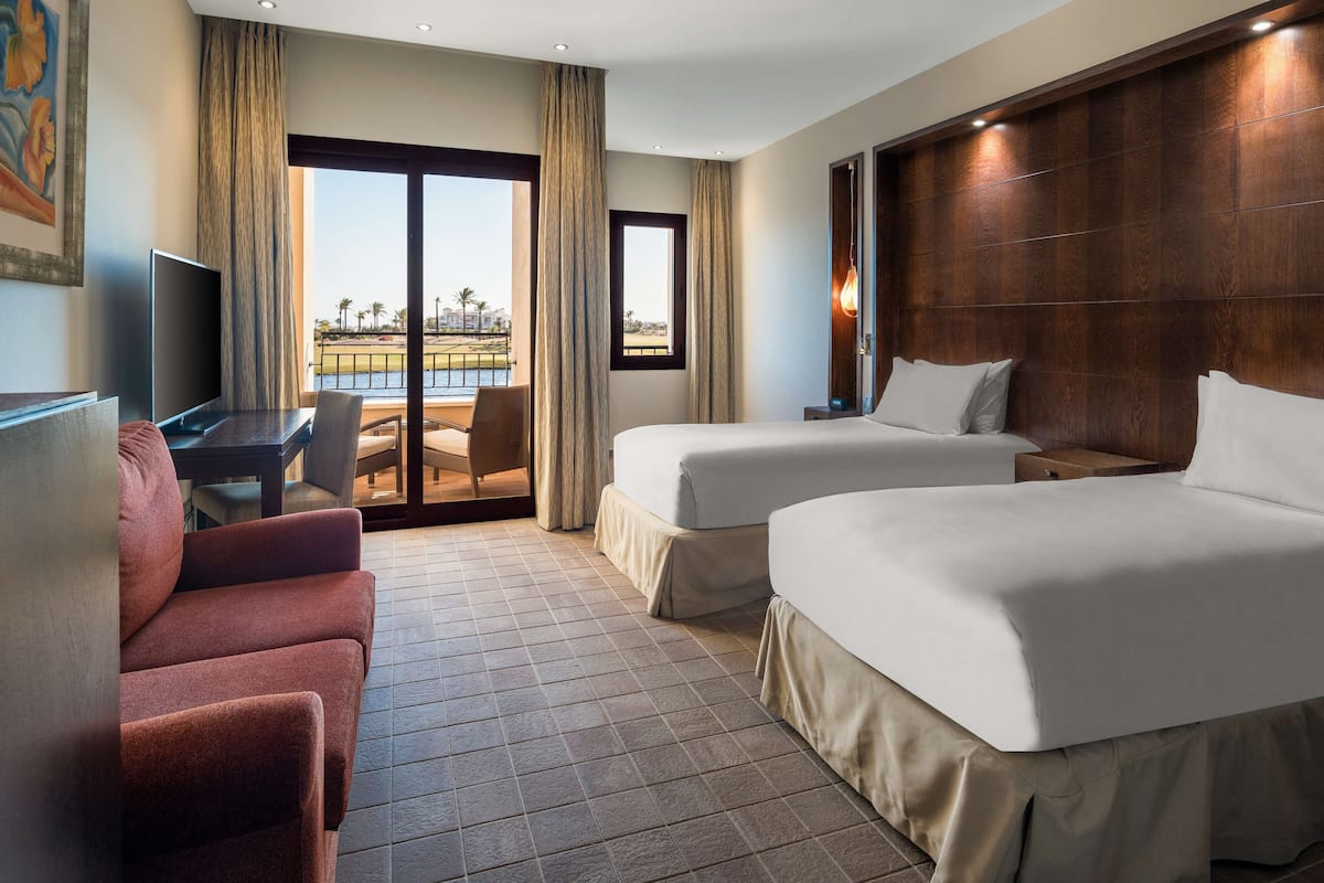 A hotel room with two beds, a sofa, a TV, and a balcony with a view.