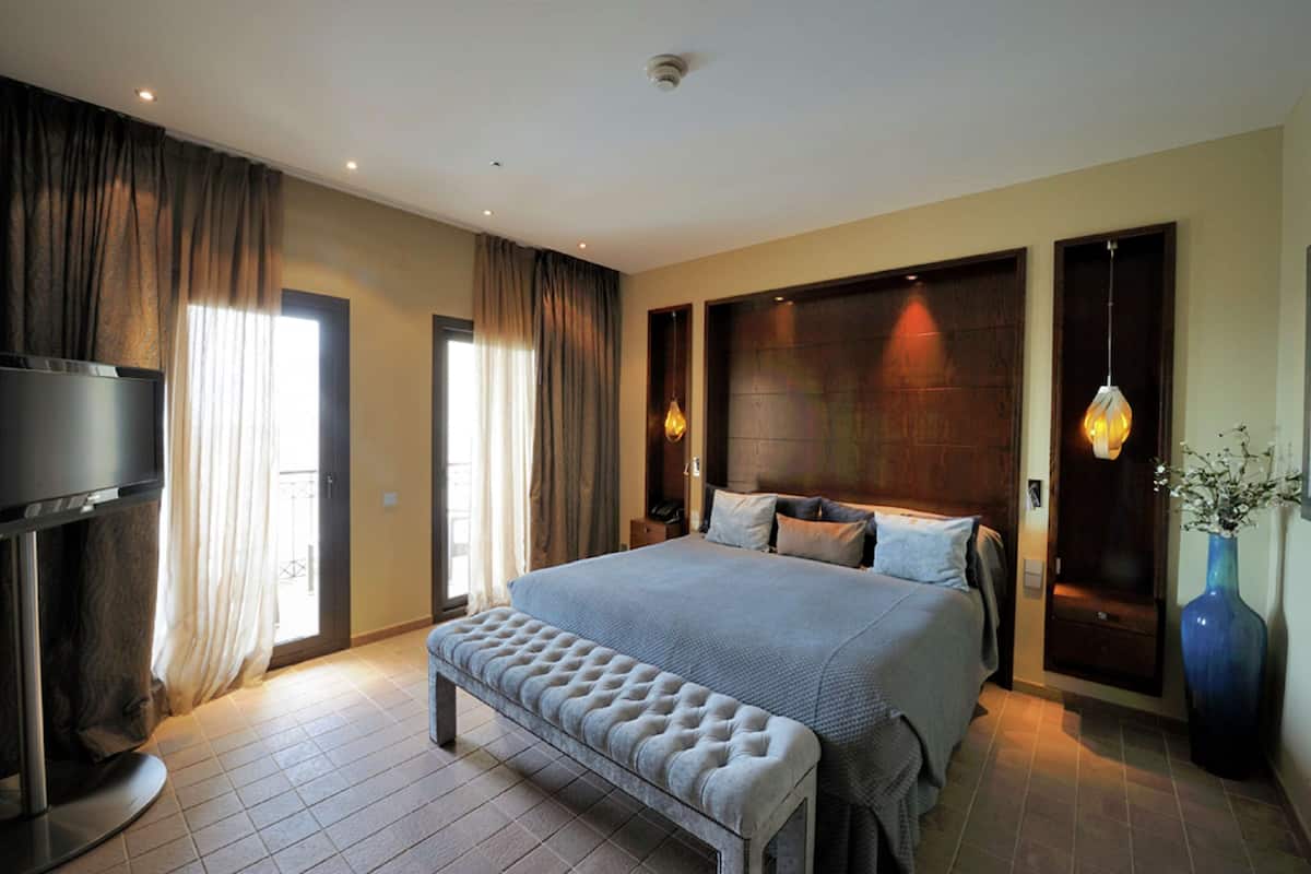 A modern bedroom with a large bed, a bench, a TV, and a vase.