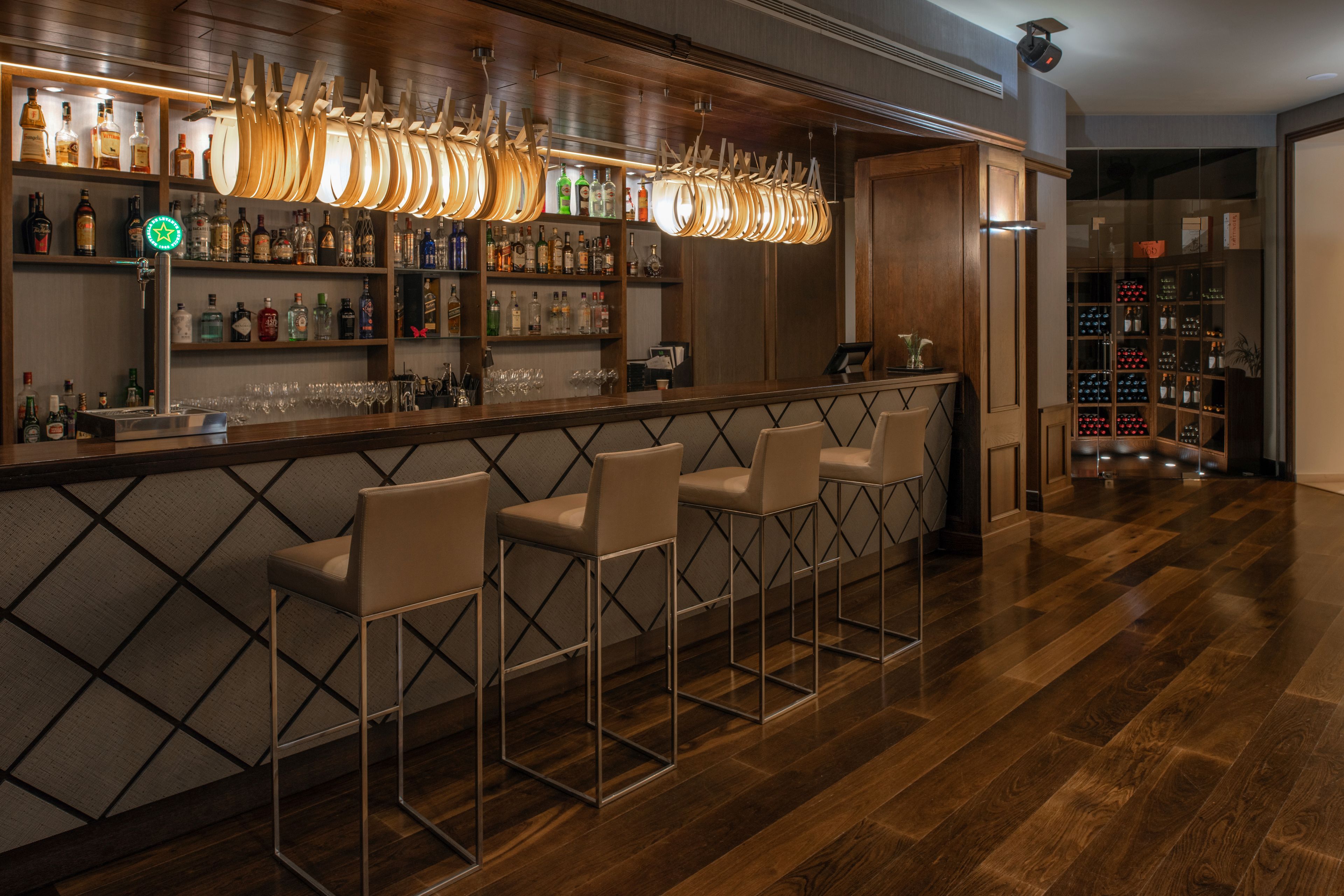 Un espace bar doté de tabourets en bois, d’une variété de bouteilles d’alcool et d’un luminaire original.