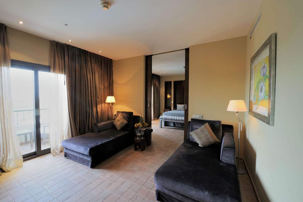 A hotel room with two dark-colored sofas, a bed, a small table with a vase, and a floor lamp.