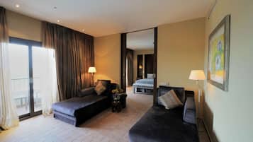 Une chambre d’hôtel avec deux canapés de couleur sombre, un lit, une petite table avec un vase et un lampadaire.