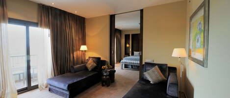 A hotel room with two dark-colored sofas, a bed, a small table with a vase, and a floor lamp.