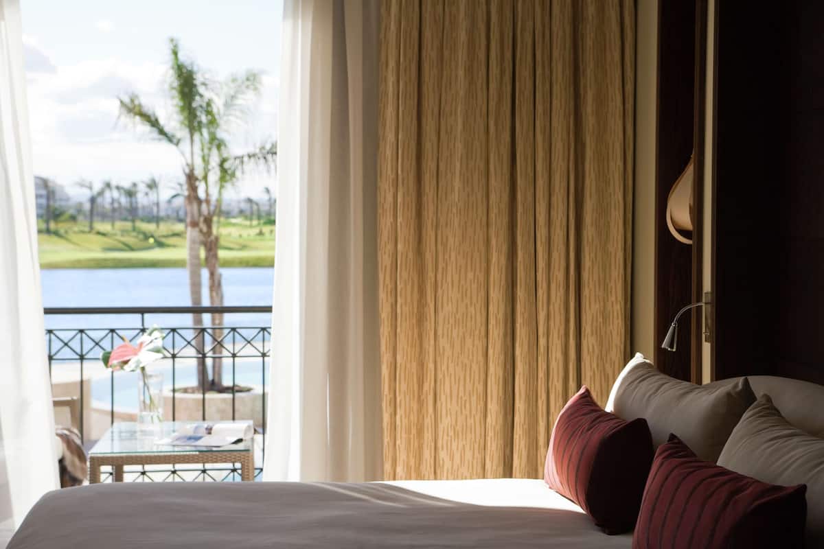 A hotel room with a bed, a table with a glass top, and a view of a golf course and water.
