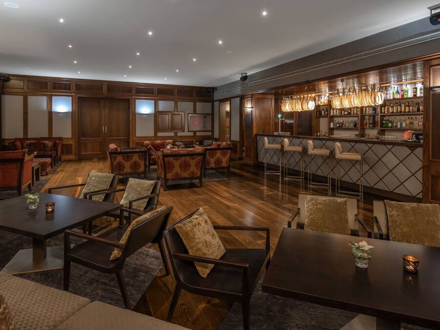A spacious lounge area with multiple seating options, a bar with a variety of bottles, and a television mounted on the wall.