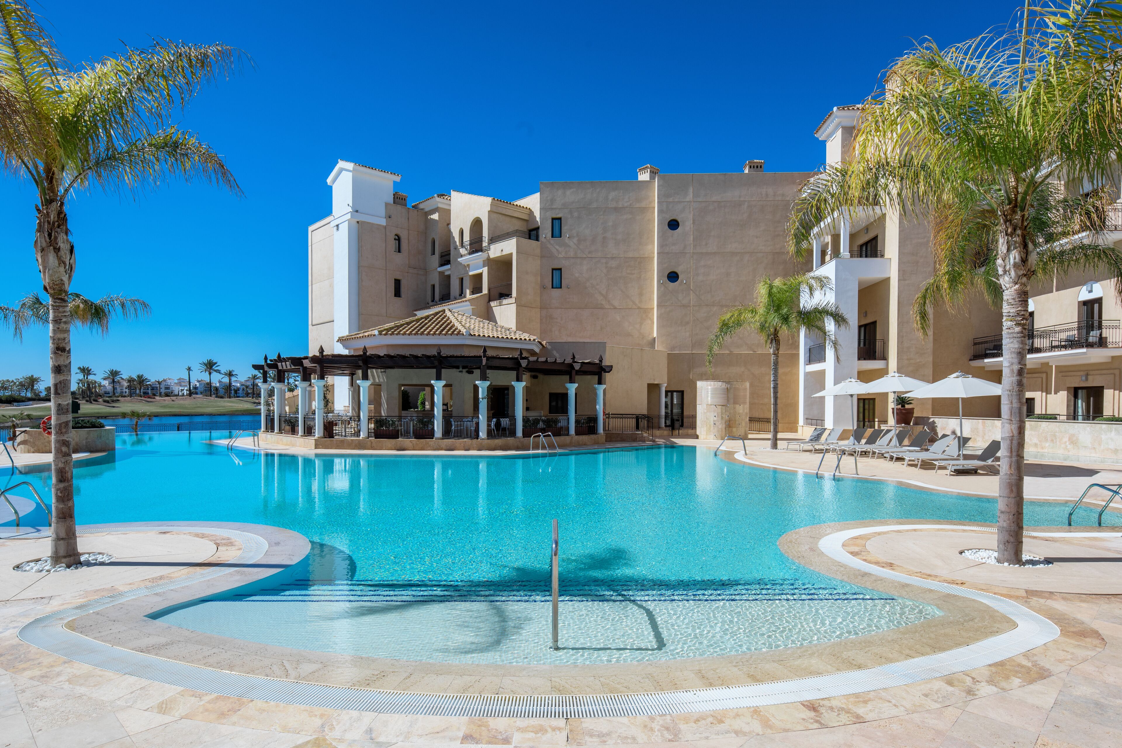 Una piscina rodeada de palmeras y un edificio con varios balcones.