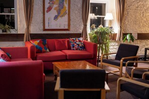 A red sofa, a wooden coffee table, and a black armchair in a room with a textured wall and a window with curtains. - Port Charlotte Youth Hostel (Islay Island)