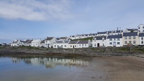 Een kustplaats met witte huizen, een rotsachtige kustlijn en kalm water dat de gebouwen weerspiegelt.