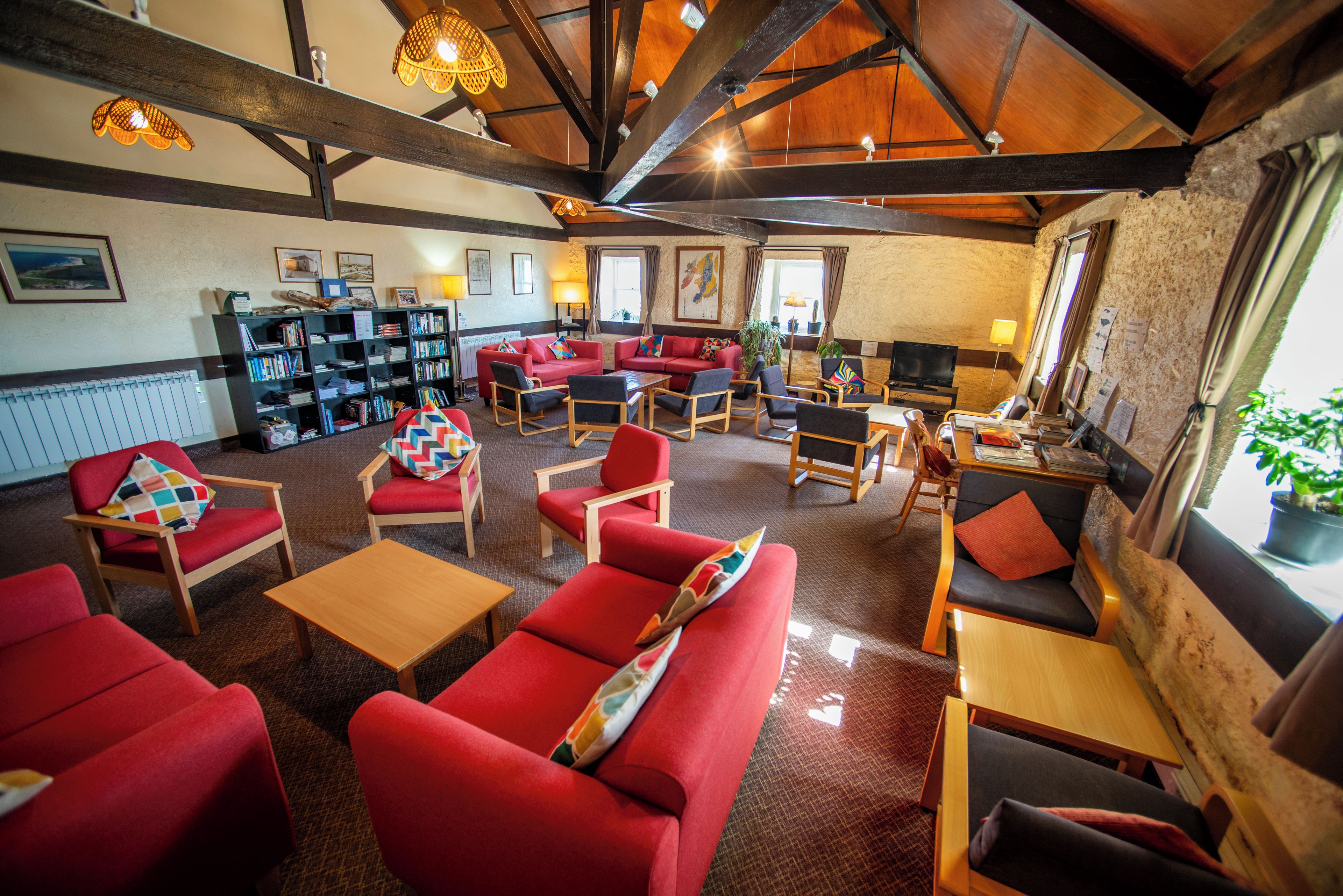 A spacious lounge area with red sofas, wooden tables, and a bookshelf filled with books.
