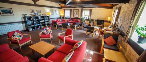 A spacious lounge area with red sofas, wooden tables, and a bookshelf filled with books.