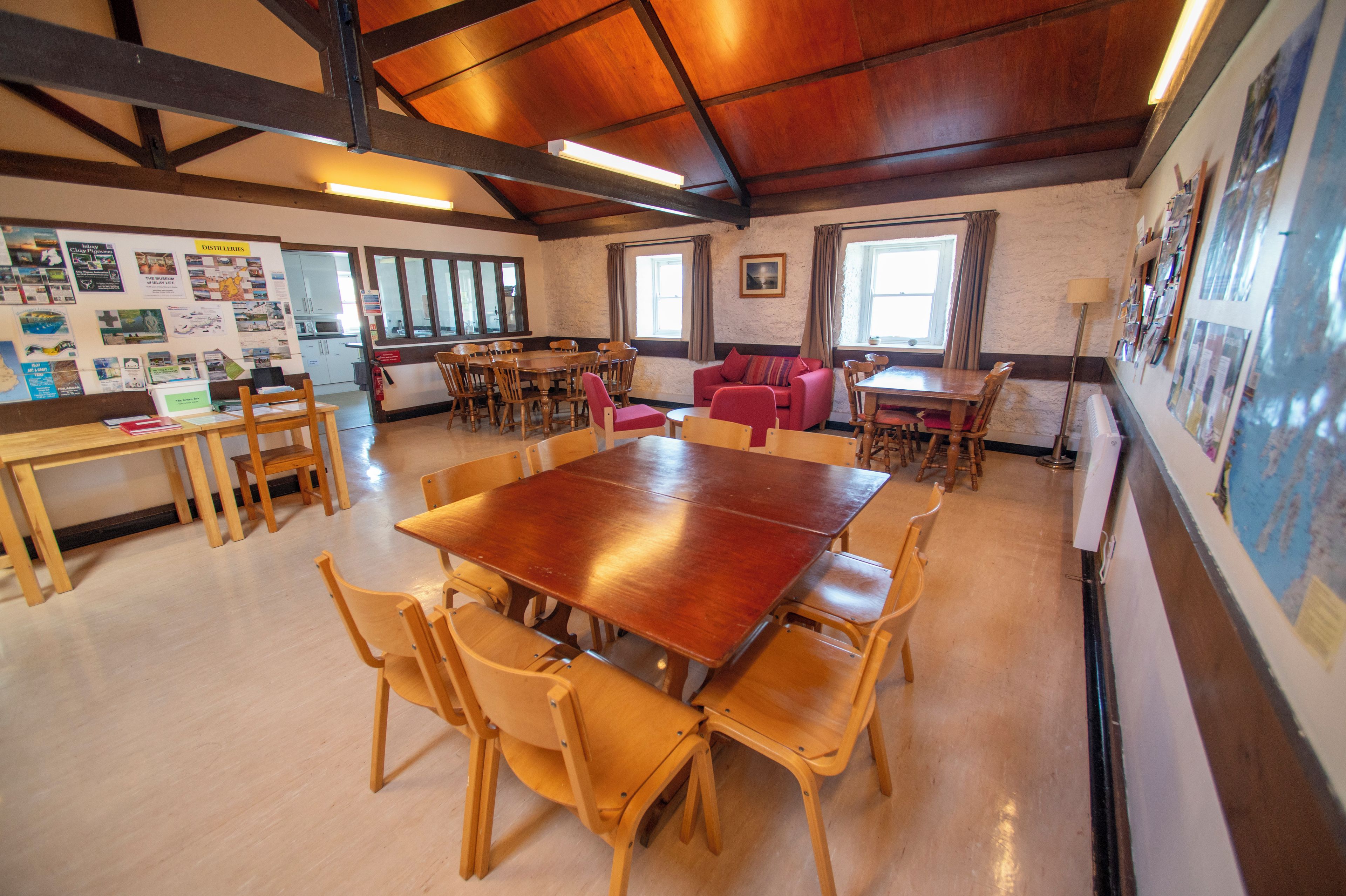 A spacious room with a large wooden table surrounded by chairs, a red sofa, and a window with curtains.