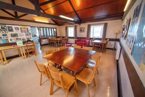 A spacious room with a large wooden table surrounded by chairs, a red sofa, and a window with curtains. - Port Charlotte Youth Hostel (Islay Island)