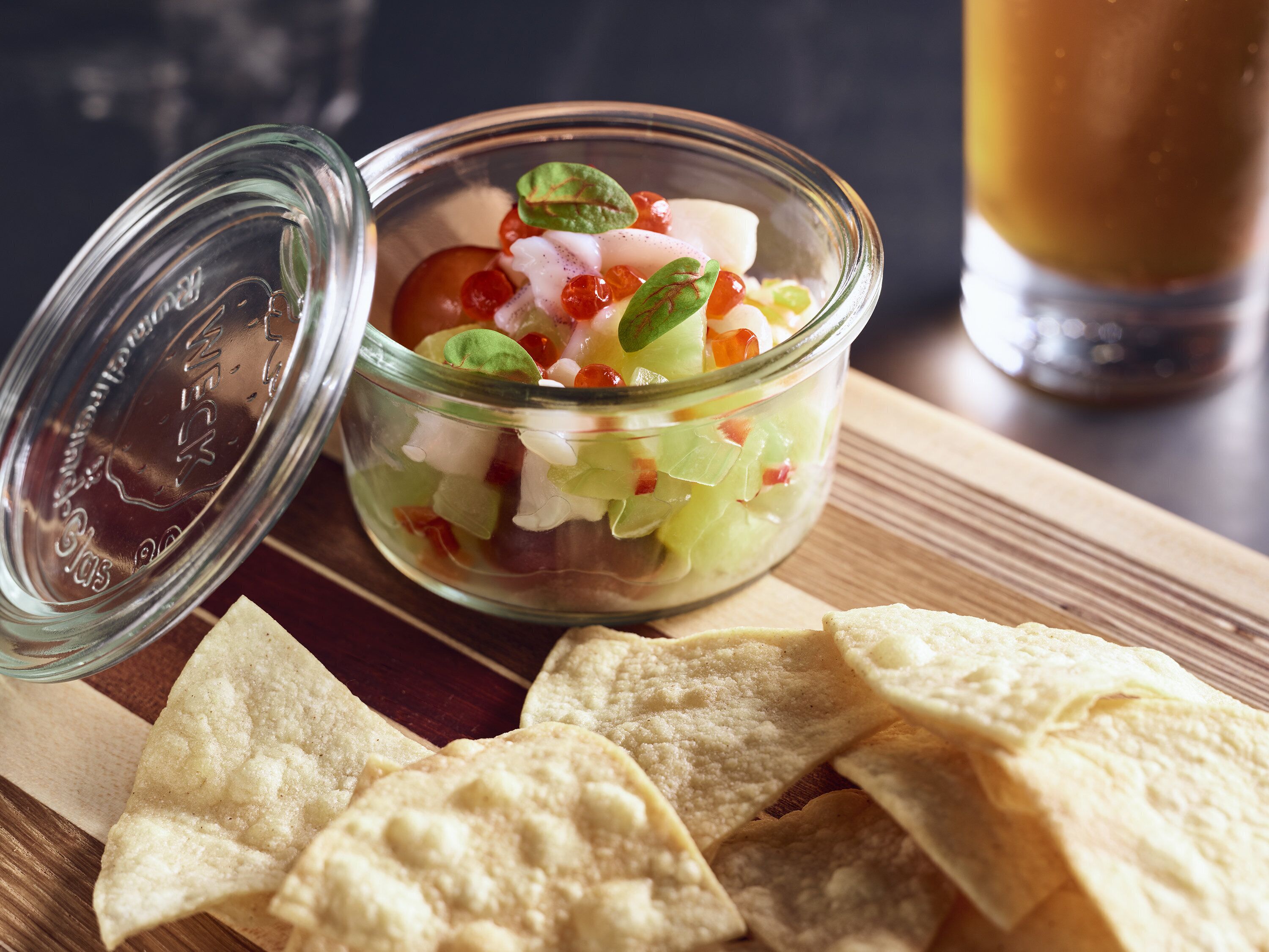 A glass bowl with a salad on a wooden surface, accompanied by tortilla chips.