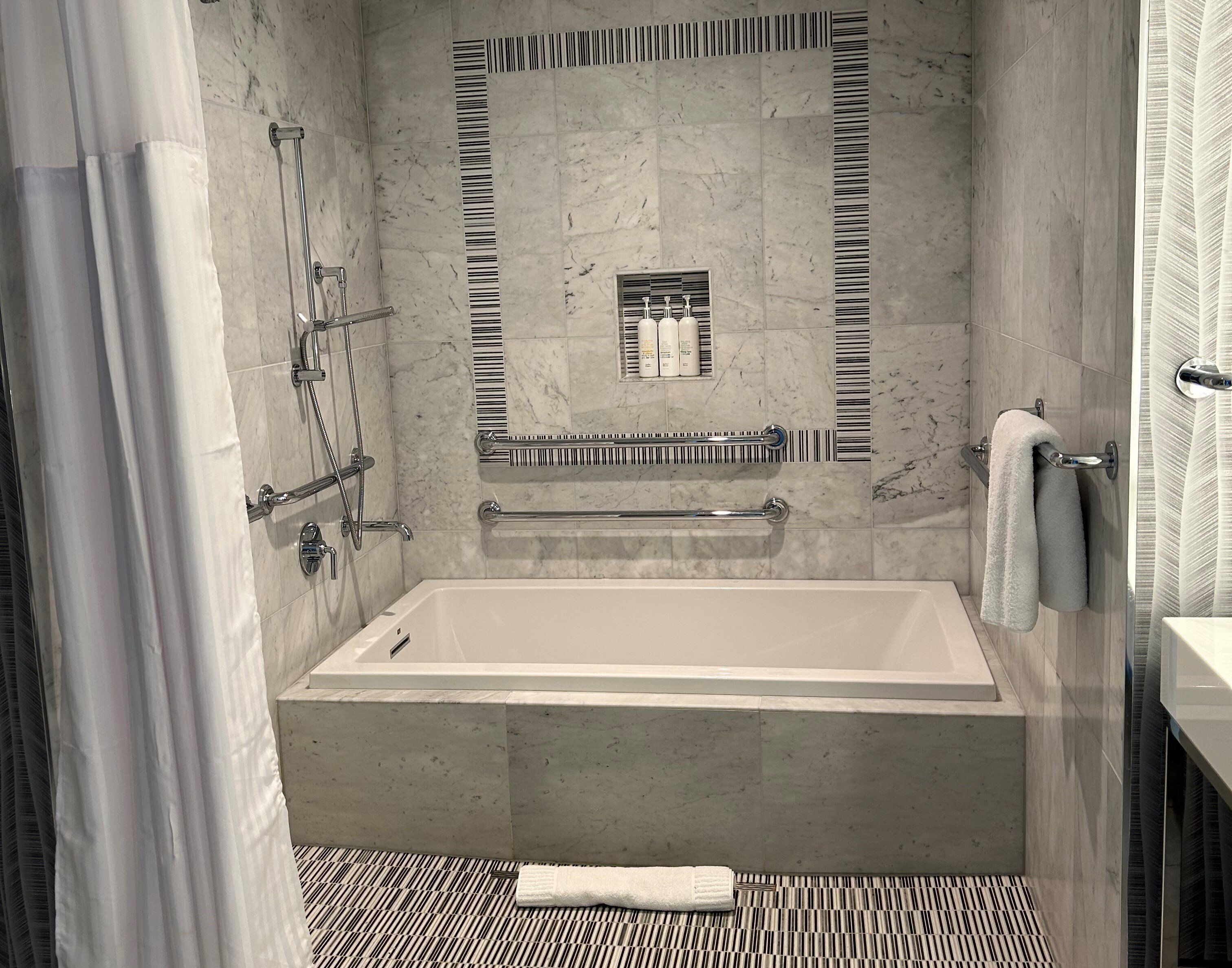 Un baño moderno con bañera, barras de apoyo y toallero.