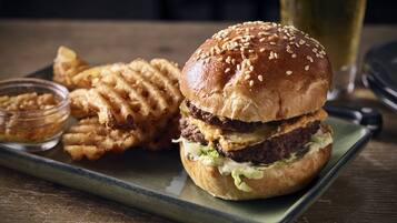 Un hamburger aux graines de sésame, servi dans un pain, accompagné de frites et d’un petit bol de sauce sur une assiette verte.