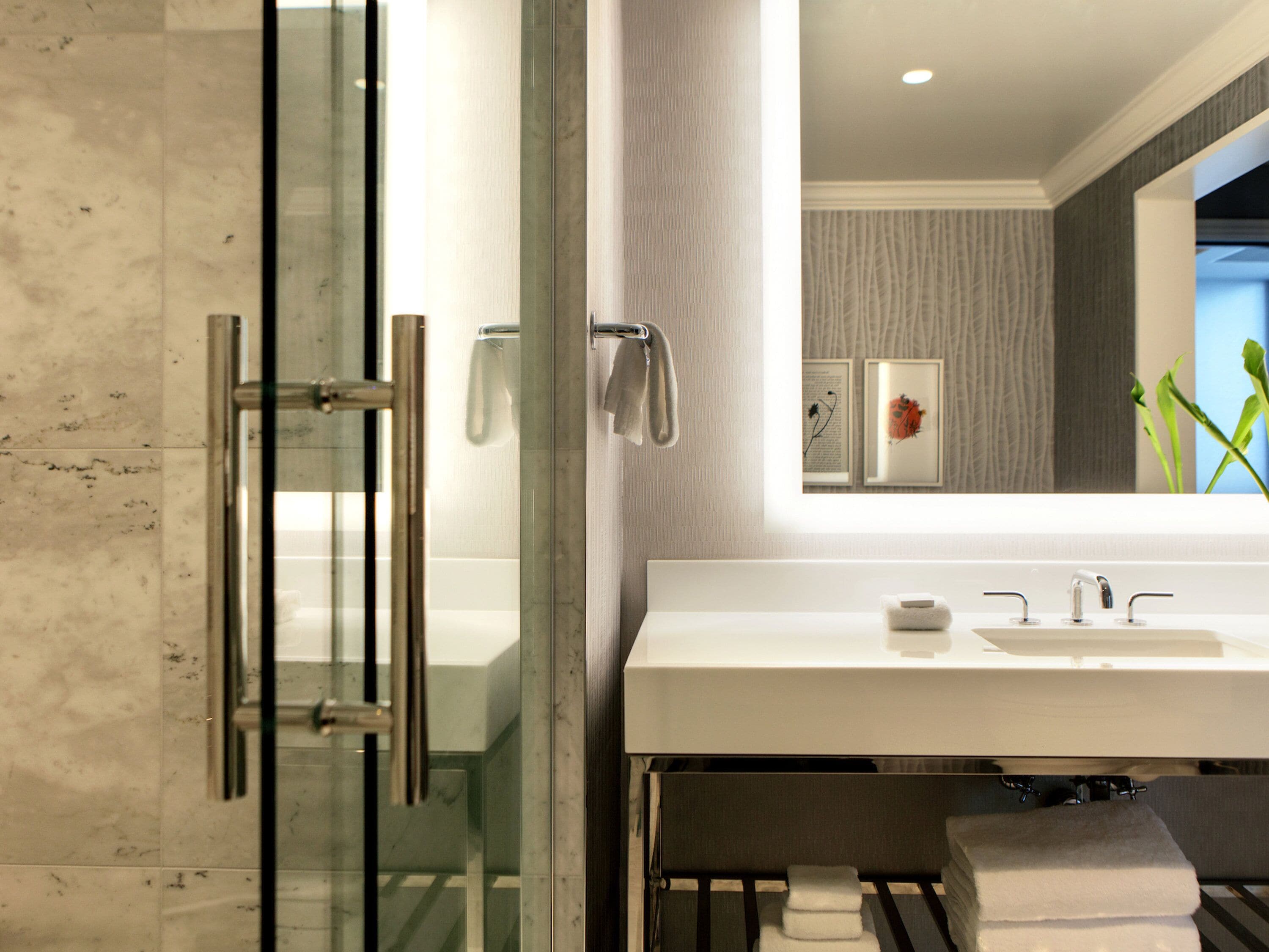 A modern bathroom with a glass shower enclosure, a white sink, and a towel rack.