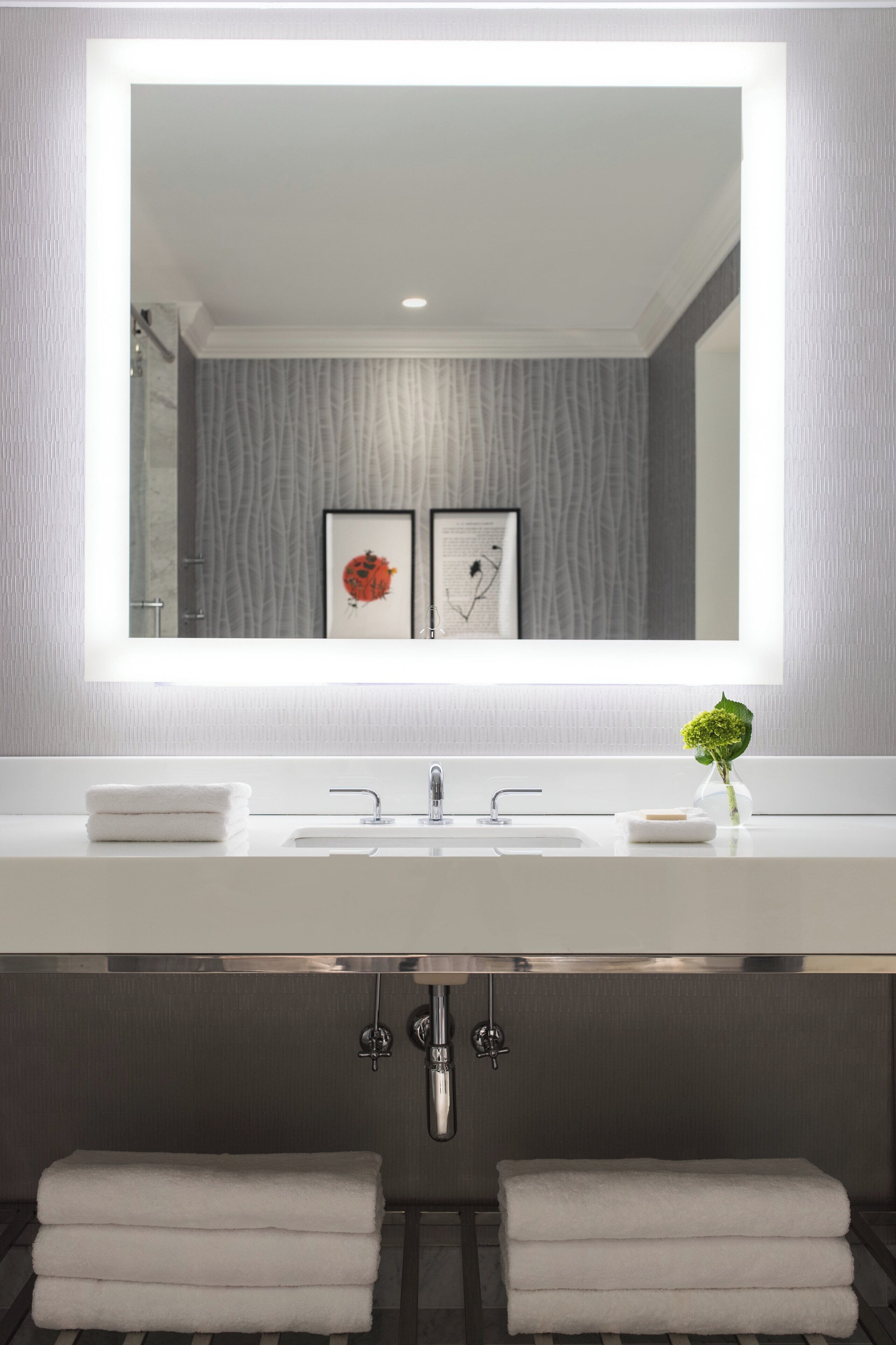 Un baño moderno con un espejo grande, un lavabo blanco y dos toallas.