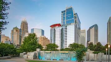 A cityscape with modern high-rise buildings, a central plaza with a water feature, and a clear sky.